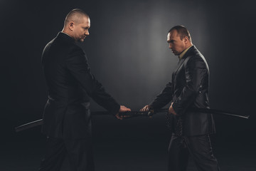 side view of businessmen taking out katana swords for fight isolated on black