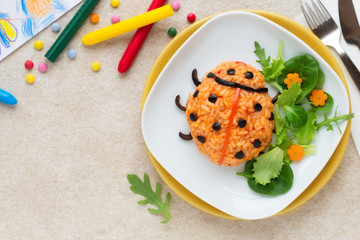 Fun food for kids - cute ladybug risotto made with tomatoes and black olives and served with fresh green salad