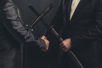 cropped shot of meeting of yakuza members in suits with katana swords isolated on black