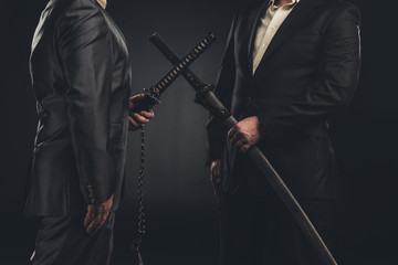 cropped shot of meeting of modern samurai in suits with katana swords isolated on black