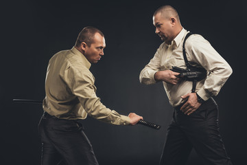 side view of men fighting with gun and katana sword on black