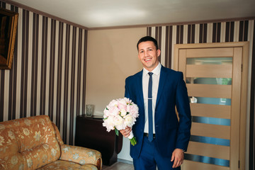 The groom is dressed at home in a suit. Cute groom posing for a photographer