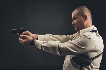 side view of man in shirt holding gun isolated on black
