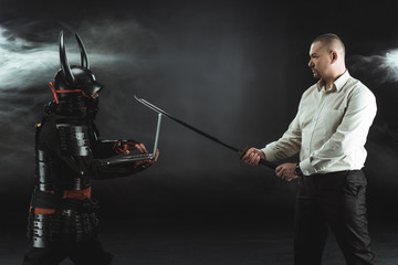 side view of man with katana standing in fornt of samurai while he using laptop
