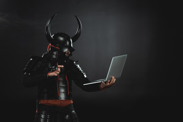 side view of armored samurai using laptop on black