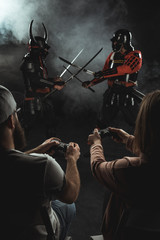 back view of man and woman playing samurai fighting in real life with gamepads on black