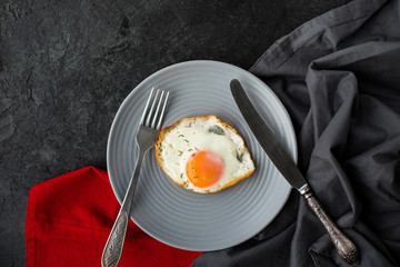 top view of fried egg on plate for breakfast with cutlery on dark surface