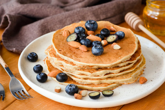Pancakes with blueberry, honey and almonds on white plate. Closeup view, selective focus