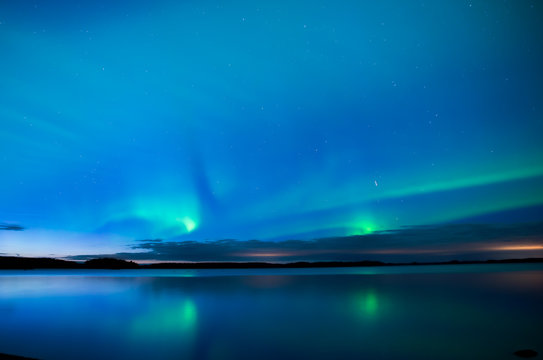 Northern lightd dancing over calm lake in Farnebofjarden national park in Sweden.