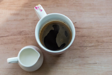 Closing a glass of freshly brewed coffee and jug of milk to an old white rustic table. Little depth of focus. Concept nostalgia.