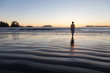 Fototapeta premium Woman Walking on a Sandy Beach during a vibrant and colorful summer sunset. Taken in Tofino, Vancouver Island, BC, Canada.