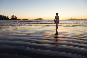 Woman Walking on a Sandy Beach during a vibrant and colorful summer sunset. Taken in Tofino, Vancouver Island, BC, Canada.
