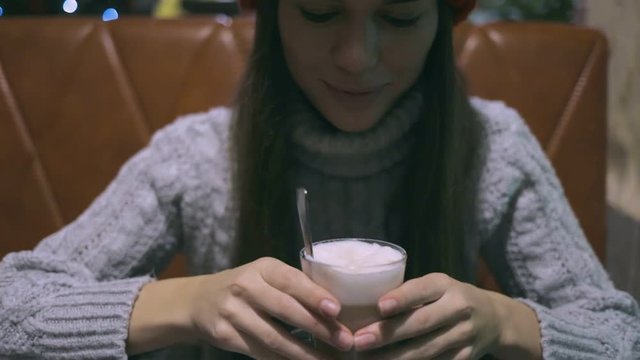 young brunette beautiful girl or young woman stiring coffee by spoon in the caffee, enjoying the taste