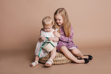 Две сестры играют вместе сидя на плетеном табурете Two sisters are playing together, sitting on wicker stool