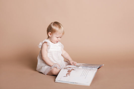 Маленькая девочка в белом платье читает большую книгу с картинками Little girl in white dress reading a large book with pictures