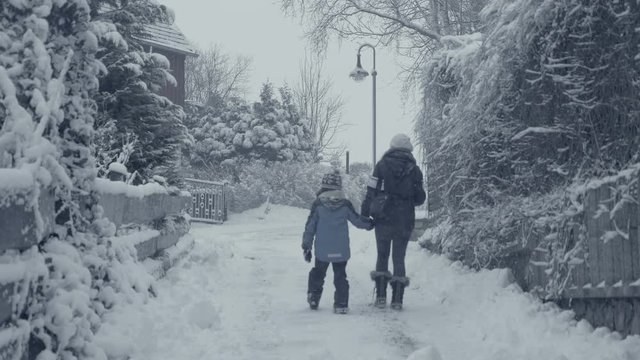 Snowy street of mountain town with walking woman and boy child, village snow calamity. Winter landscape, falling snow. Everything is covered, fresh powder. Winter atmosphere, Christmas background.