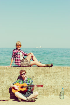 Young man playing guitar to his girlfriend by seaside