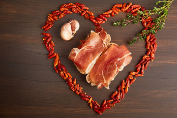 Red hot pepper is lined in the form of heart. A branch of thyme, a clove of garlic. Sandwiches made from hand-made rye bread and thin chopped fresh bacon.