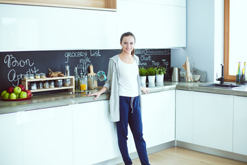 Young woman with orange juice and tablet in kitchen.