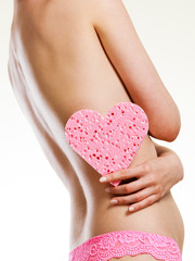 Naked woman holding pink heart shaped sponge in hand