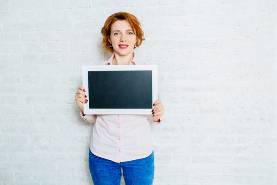 Portrait of a mature red hair business woman holding a shalk board over white wall background.