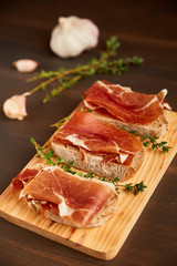 Sandwiches made from hand-made rye bread and thin chopped fresh bacon. Fresh green thyme on a wooden board. Succulend bacon on a wooden table.