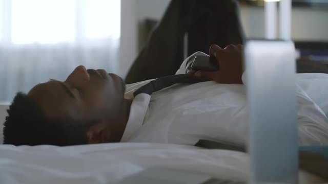 African businessman in shirt falling on comfortable bed and resting in hotel room