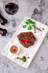 Top view grilled beef steak with rosemary, herbs and spices on gray concrete background. and glass of red wine on table, restaurant kitchen concept
