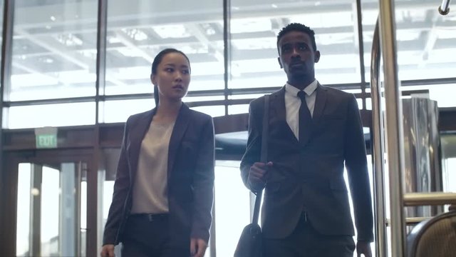 Asian businesswoman and African businessman entering hotel and walking together through lobby