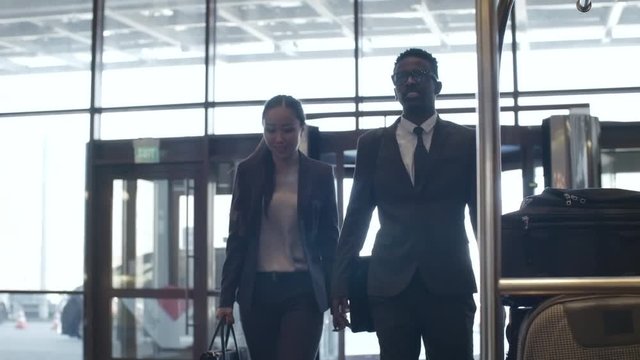 Asian businesswoman and African businessman walking together through lobby in hotel and talking