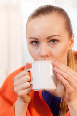 Woman lying on sofa under blanket drinking tea