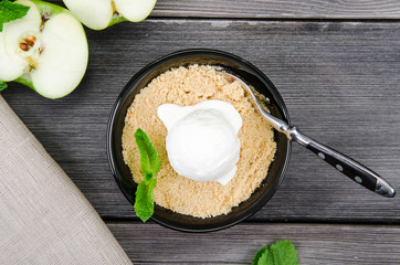 Top view close up Apple crumble dessert with vanilla ice cream, green mint on grey wooden table background. fork in cake on tablecloth