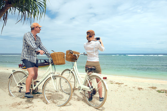 Happy couple taking pictures looks at sea standing near their old fashioned bicycles on theon beach.