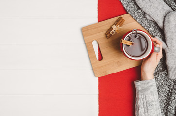 Female hand holding a cup of tea or coffee on white wooden table. Winter or christmas cosy background. Photograph taken from above, top view with copy space