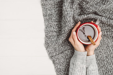 Female hand holding a cup of tea or coffee on white wooden table. Winter or christmas cosy background. Photograph taken from above, top view with copy space