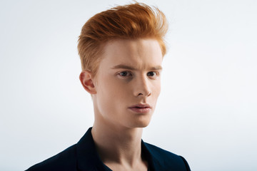 Cute. Good-looking serious red-haired young man wearing a black jacket and staring and having a modern haircut