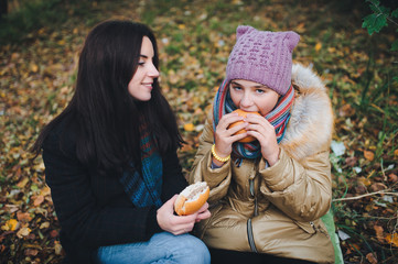 Mother and daughter eating hamburgers at a picnic in the autumn park.