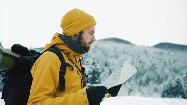 Beautiful mountains in winter time. Man with beard, wearing yellow winter clothes goes with a tourist map in hands, against the background of the winter landscape