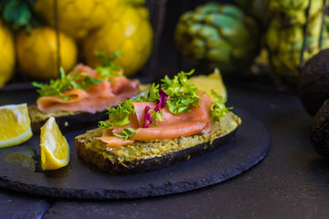 morning breakfast with hot coffee and a sandwich with avocado, soft cheese, lemon and red fish trout on a dark background