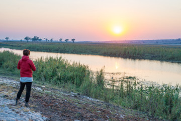 Fototapeta na wymiar Tourist looking at sunrise over Chobe River, Namibia Botswana Africa. Natural colors, rear view.