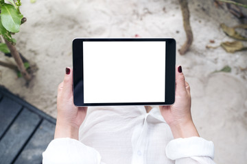 Mockup image of a woman's hand holding black tablet pc with blank white desktop screen with sand and beach background