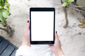 Mockup image of a woman's hand holding black tablet pc with blank white desktop screen with sand and beach background
