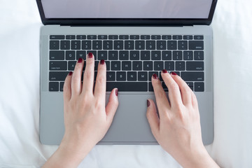 Top view closeup image of woman's hands typing on laptop on the bed in bedroom