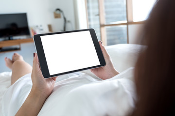 Mockup image of woman's hands holding black tablet pc with blank desktop white screen while lying in a white bed