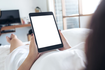 Mockup image of woman's hands holding black tablet pc with blank desktop white screen while lying in a white bed