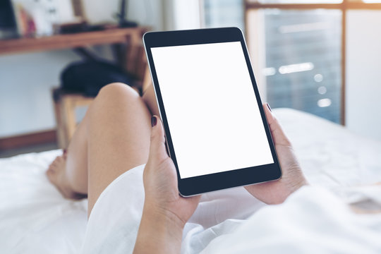 Mockup image of woman's hands holding black tablet pc with blank desktop white screen while lying in a white bed with feeling relaxed