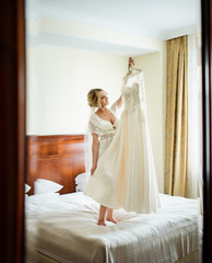 Beautiful blonde bride stands with a wedding dress in the room