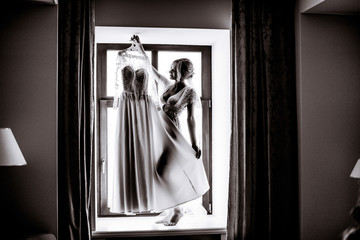 Black and white picture of stunning bride standint on the windowsill with wedding dress