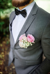 Handsome bearded groom in grey suit with pink boutonniere poses in the park