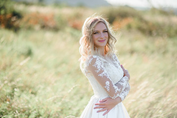 Fototapeta premium Stunning bride with white curls stands on the field in a sunny day